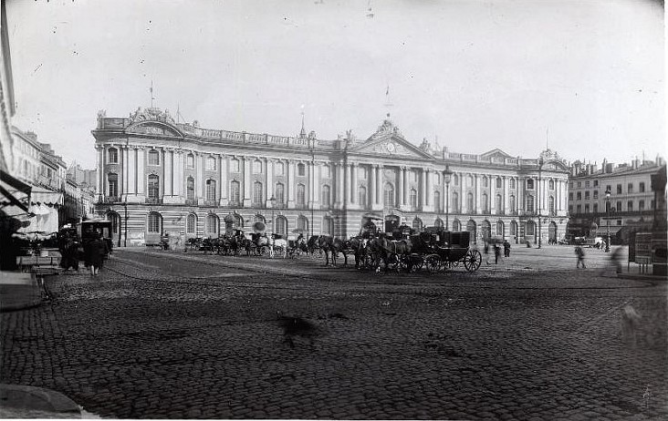 Toulouse (Haute-Garonne), hôtel de ville appelé Capitole. Référence : Place du Capitole. Fin 19e siècle. Vue d'ensemble de la place prise depuis l'angle nord-ouest. Au milieu plusieurs voitures à cheval, au fonds la façade de l'hôtel de ville. Archives municipales de Toulouse (reproduction), Domaine public. Toulouse (Haute-Garonne), hôtel de ville appelé Capitole. Référence : Place du Capitole. Fin 19e siècle. Vue d'ensemble de la place prise depuis l'angle nord-ouest. Au milieu plusieurs voitures à cheval, au fonds la façade de l'hôtel de ville. Archives municipales de Toulouse (reproduction), Domaine public.